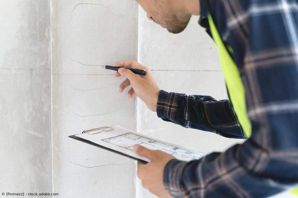 Eine Person markiert mit einem Bleistift Maße an einer Wand, während sie ein Klemmbrett und ein Lineal hält.