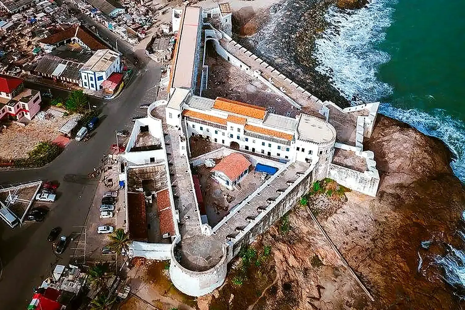 Pueblo ribereño al atardecer, con barcos de madera, casas sobre pilotes y un alto templo desértico reflejados en el agua
