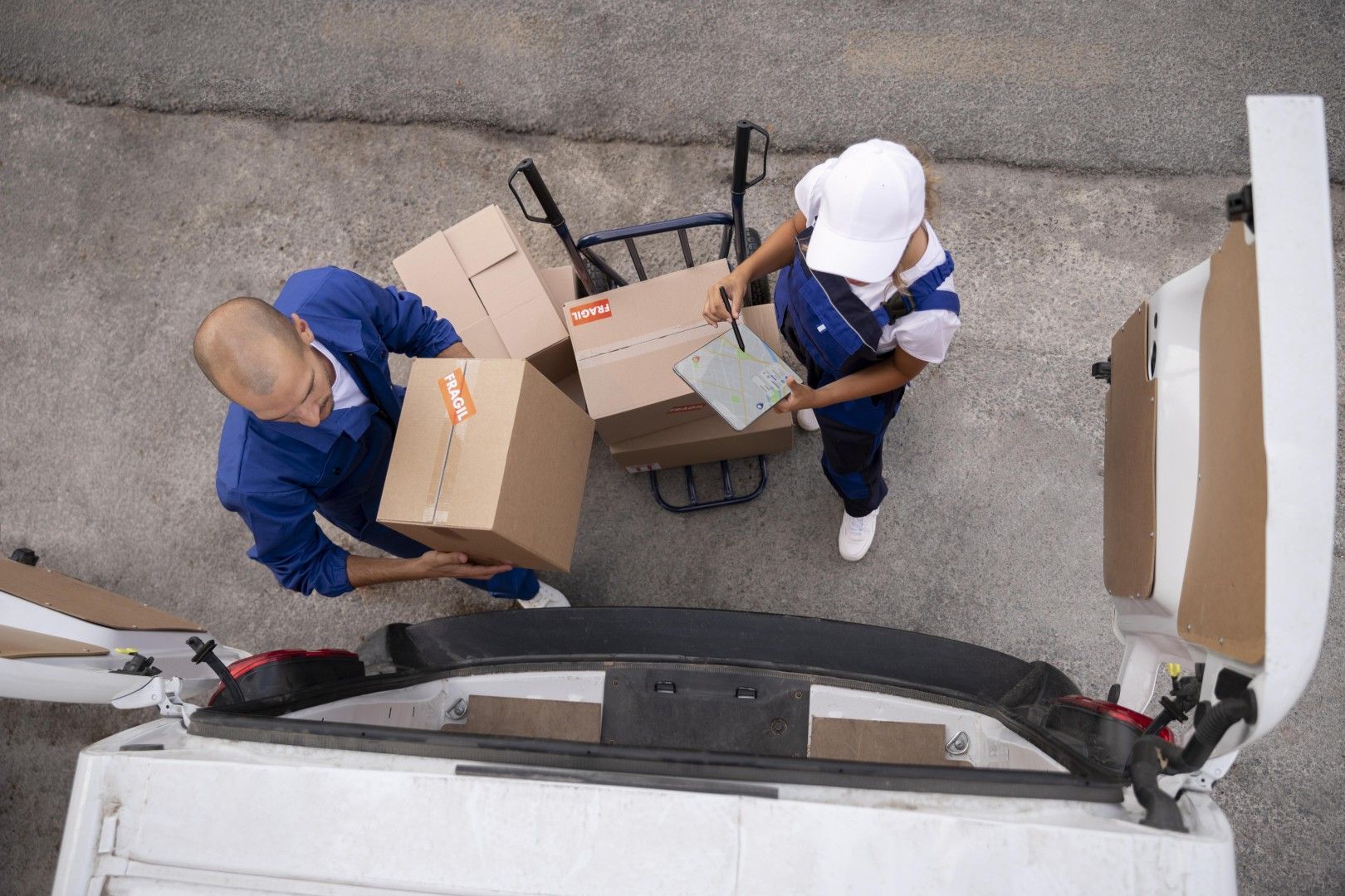 Dos operarios de mudanzas transportando cajas de cartón junto a un camión en una calle vista desde arriba