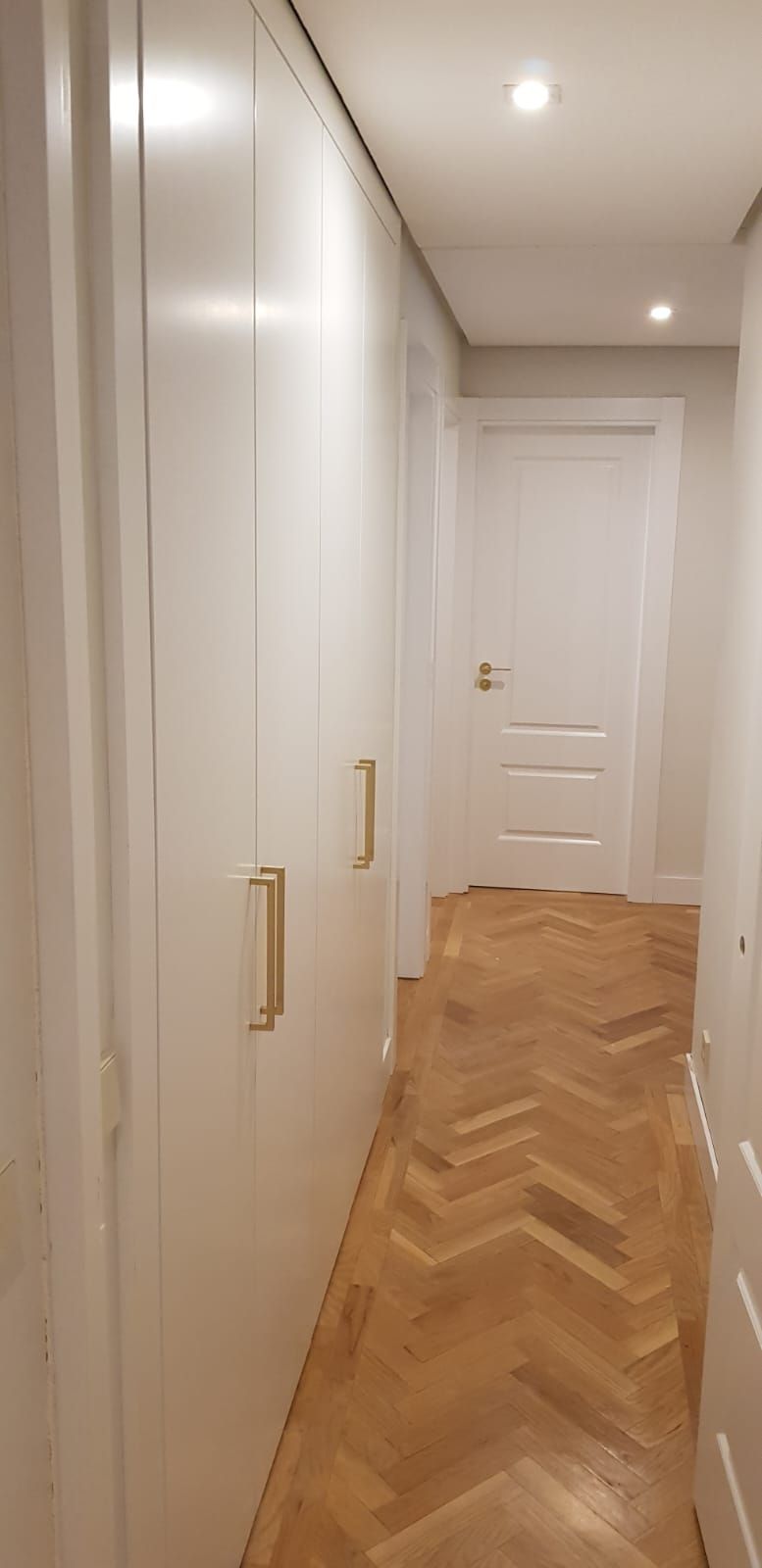 Un pasillo largo con piso de madera y armarios blancos.