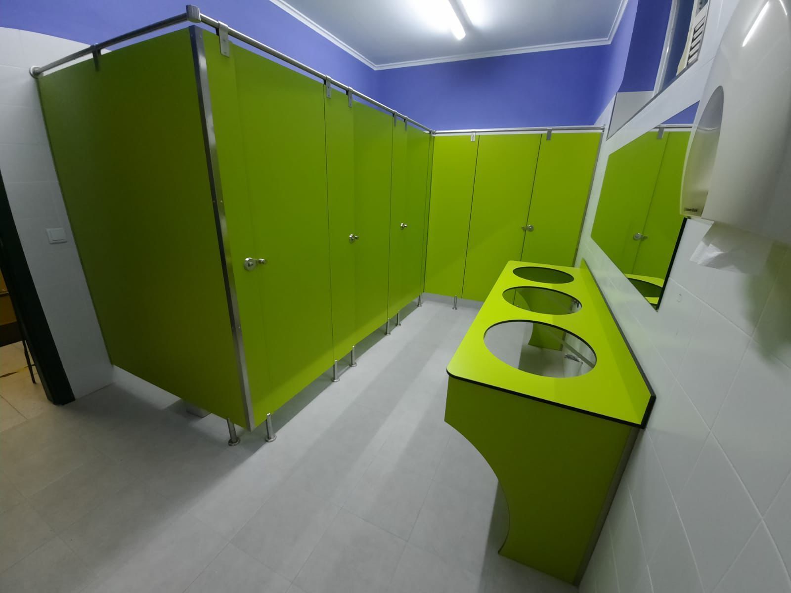 Un baño con cubículos verdes y un lavabo amarillo.