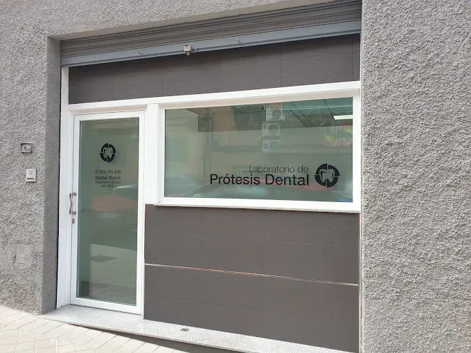 Fachada de un laboratorio dental con paredes grises, puerta de cristal y letrero en la ventana que dice