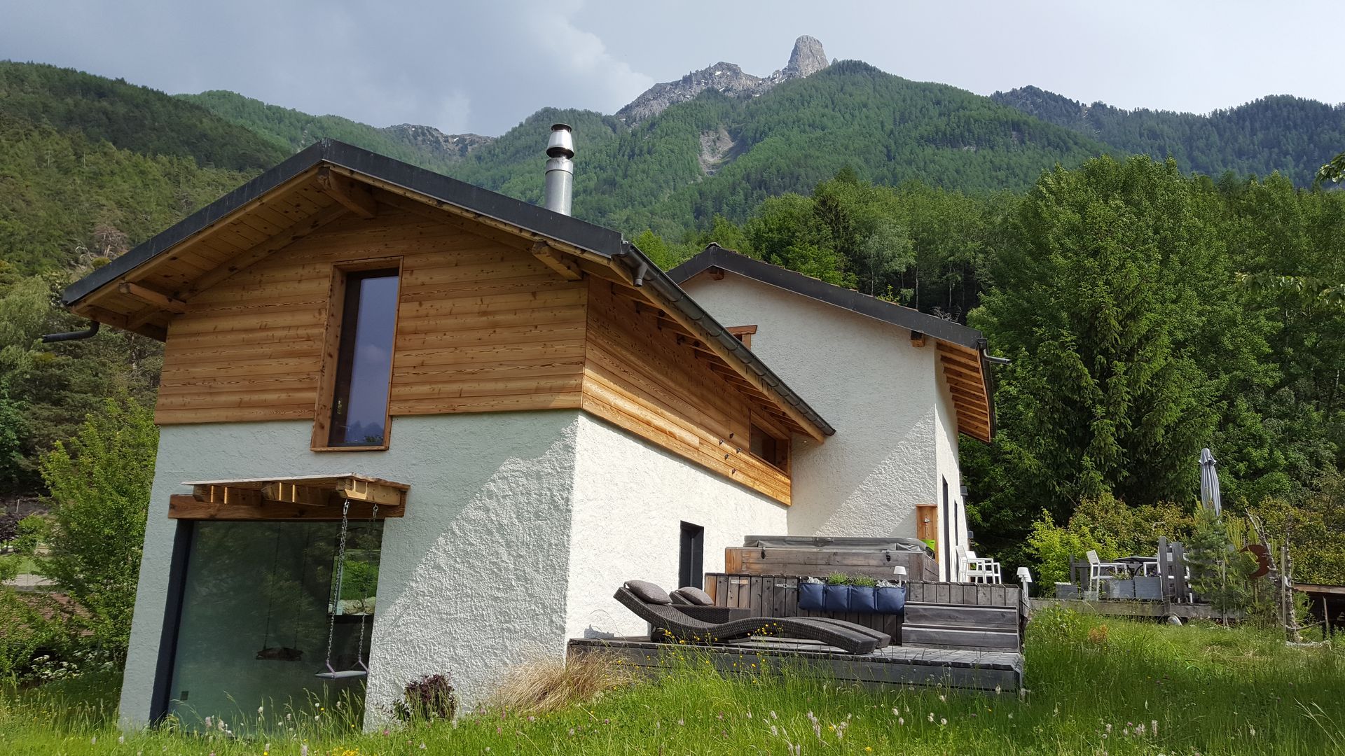 Une maison blanche avec un toit en bois est entourée d'arbres et de montagnes.
