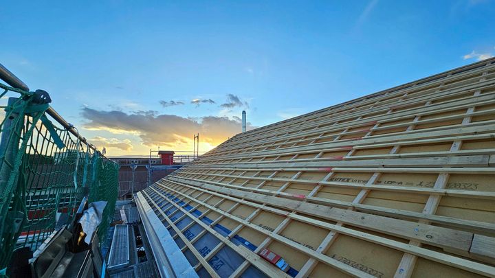 Auf einem im Bau befindlichen Gebäude wird ein Holzdach errichtet.