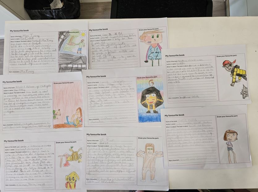 Hojas de trabajo de los alumnos expuestas, con texto manuscrito y dibujos coloridos, dispuestas sobre una mesa.