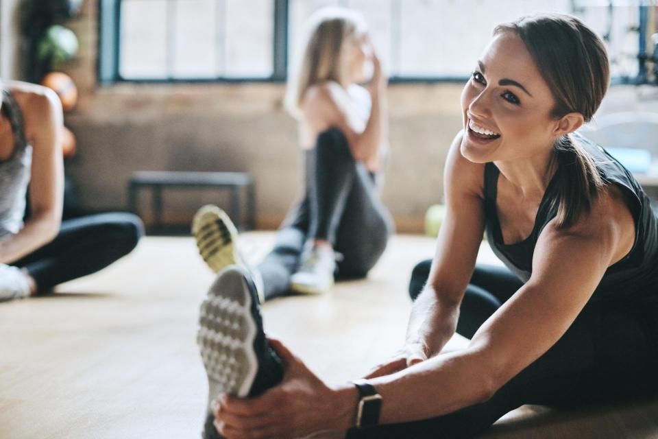 PV Gesundheitstraining - Frau in Sportkleidung sitzt auf dem Boden und streckt und massiert ihr Bein