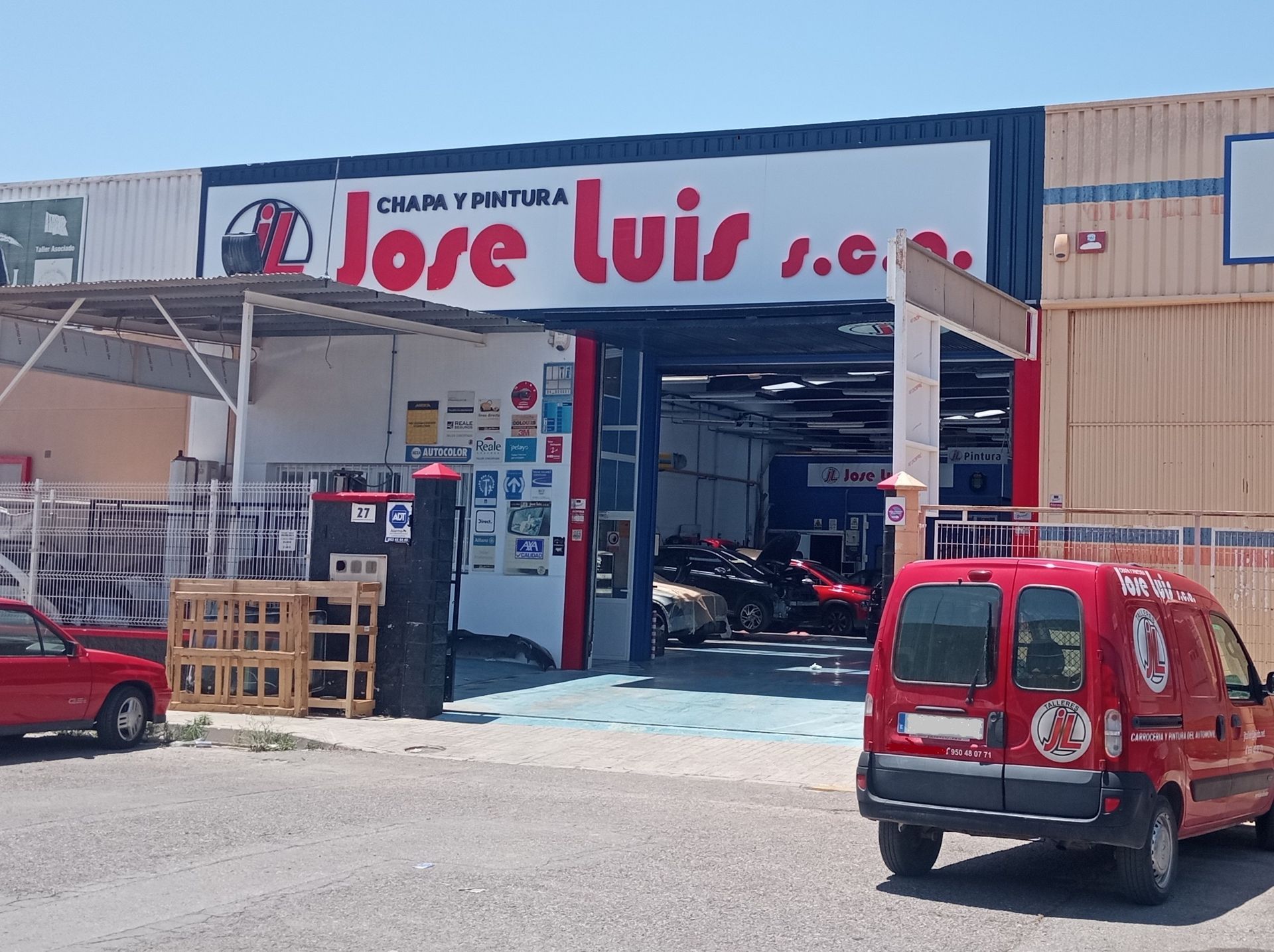 Un coche rojo está estacionado frente a una tienda llamada José Luis.