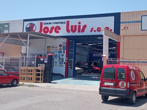 Un coche rojo está estacionado frente a una tienda llamada José Luis.