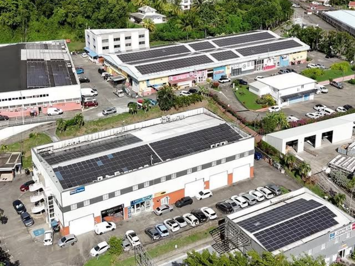 Vue aérienne de bâtiments commerciaux avec des panneaux solaires sur les toits, voitures garées à l'extérieur.