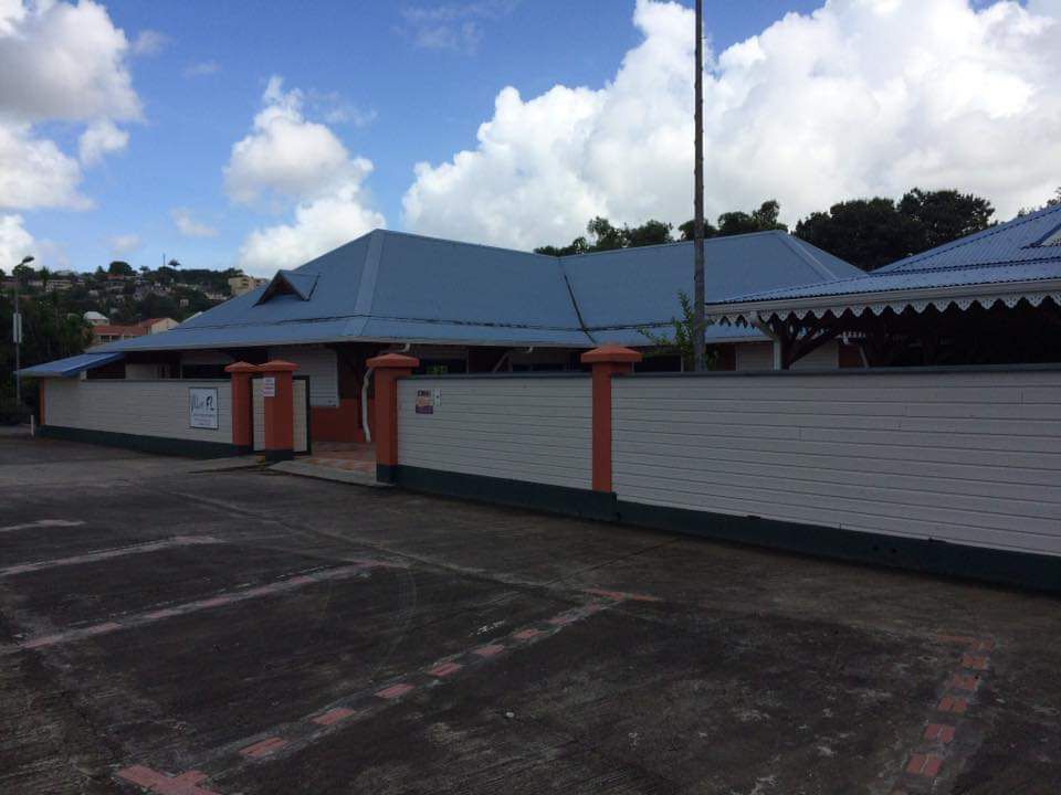 Bâtiment au toit bleu et au mur blanc, sur fond de ciel nuageux.