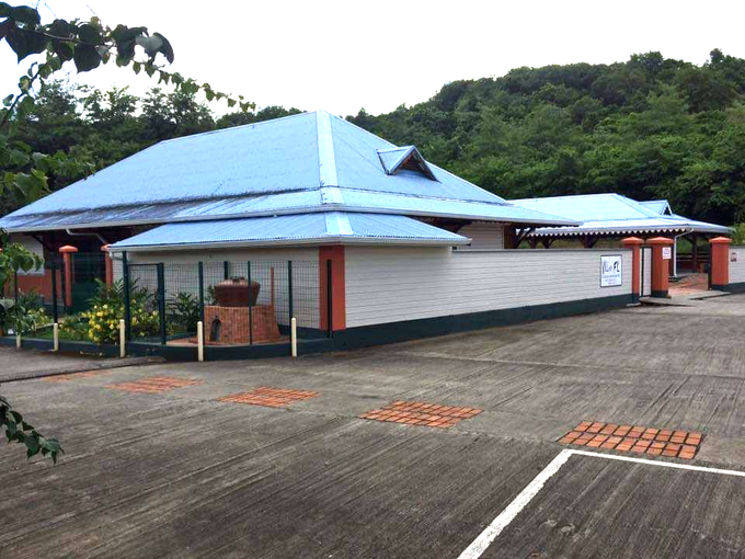 Bâtiment avec un toit bleu, des murs blancs et des garnitures orange, sur fond d'arbres verts.