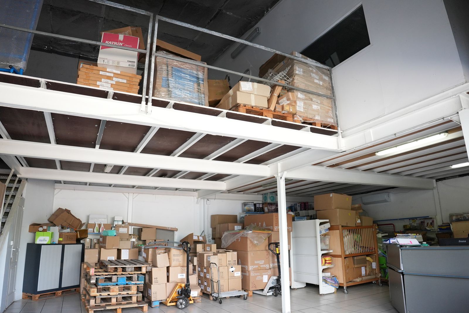 Intérieur d'entrepôt avec zone de stockage en mezzanine, rempli de cartons et de palettes.