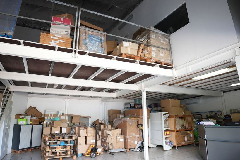 Intérieur d'entrepôt avec zone de stockage en mezzanine, rempli de cartons et de palettes.