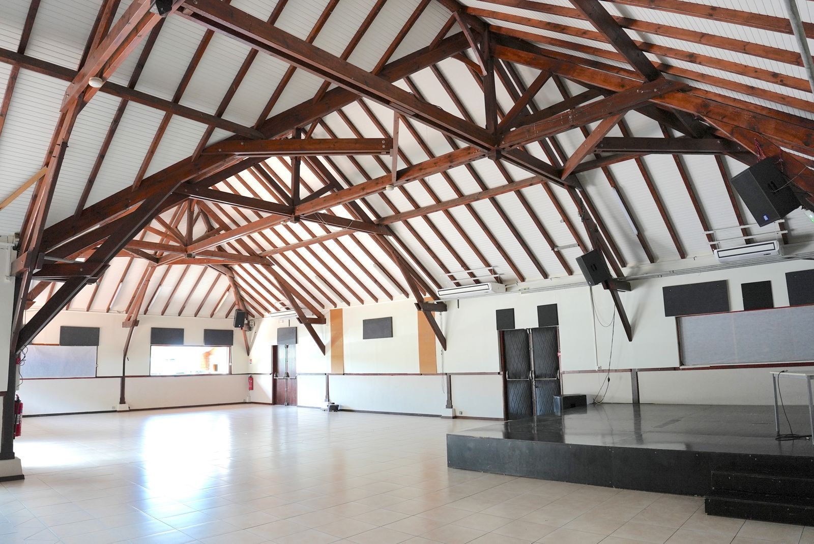 Intérieur d'une grande salle ouverte avec un plafond à poutres en bois, des murs blancs et une scène.