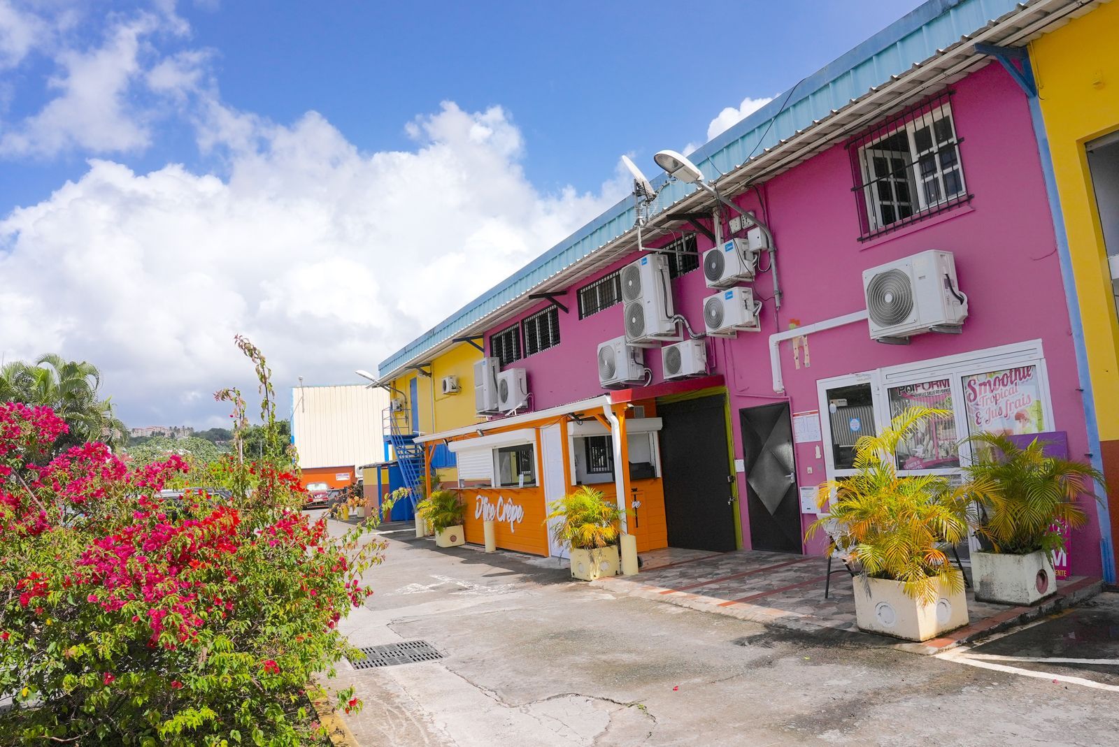 Bâtiments colorés en rose vif et jaune avec des unités de climatisation et un ciel nuageux.