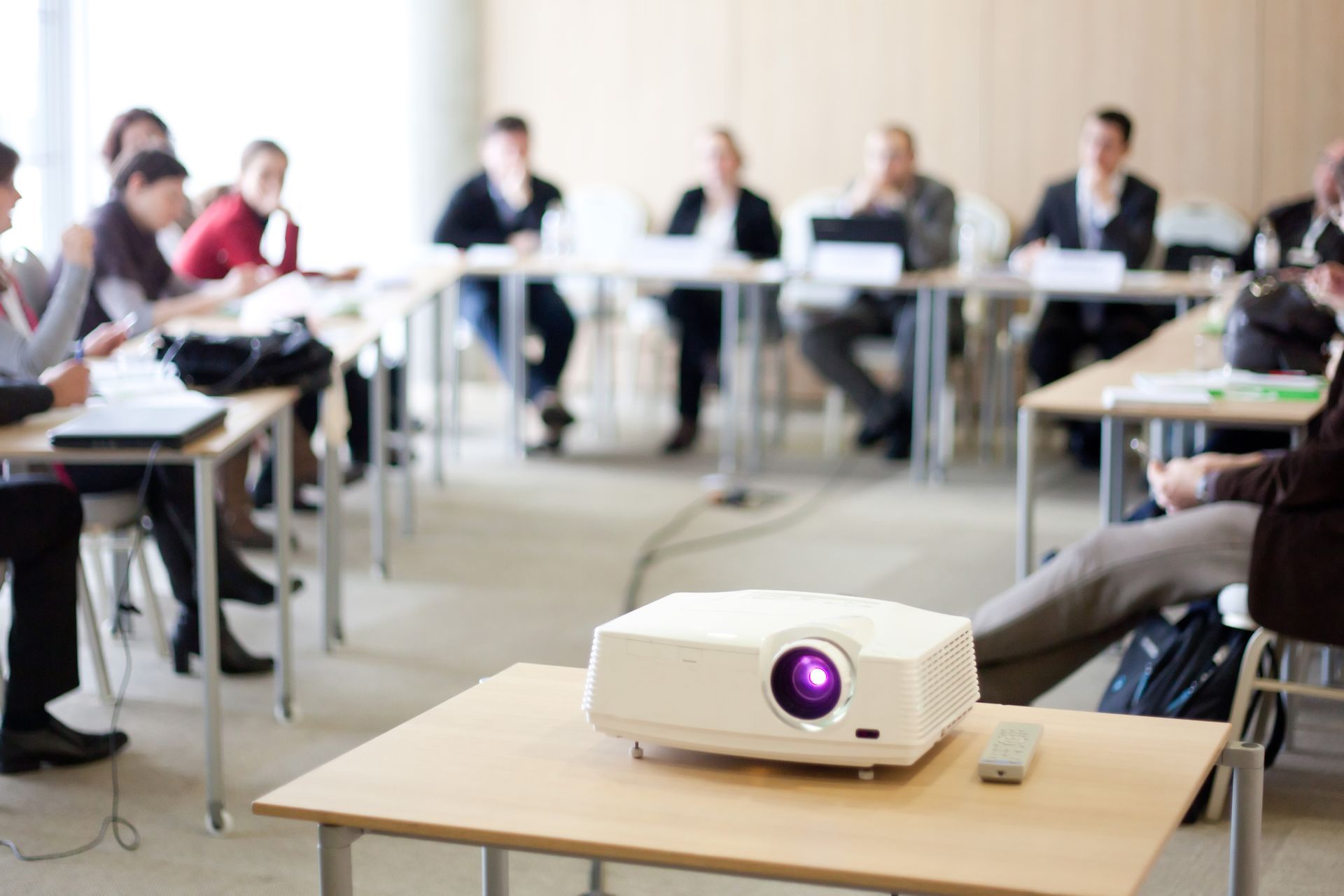 Projecteur sur table, personnes en réunion, utilisant des ordinateurs portables, dans une salle de classe.