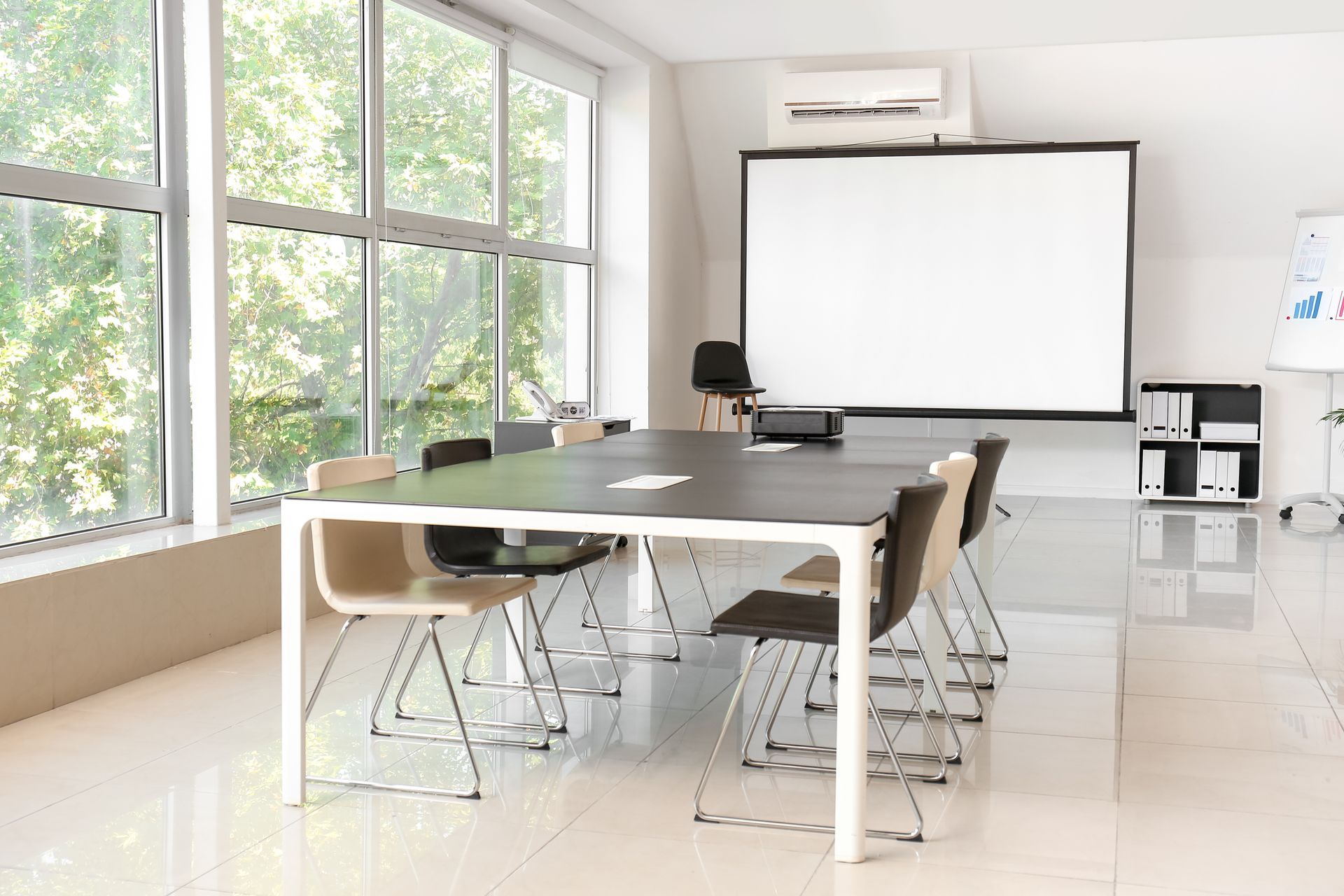 Salle de conférence avec longue table, chaises, écran de projection et grandes fenêtres.