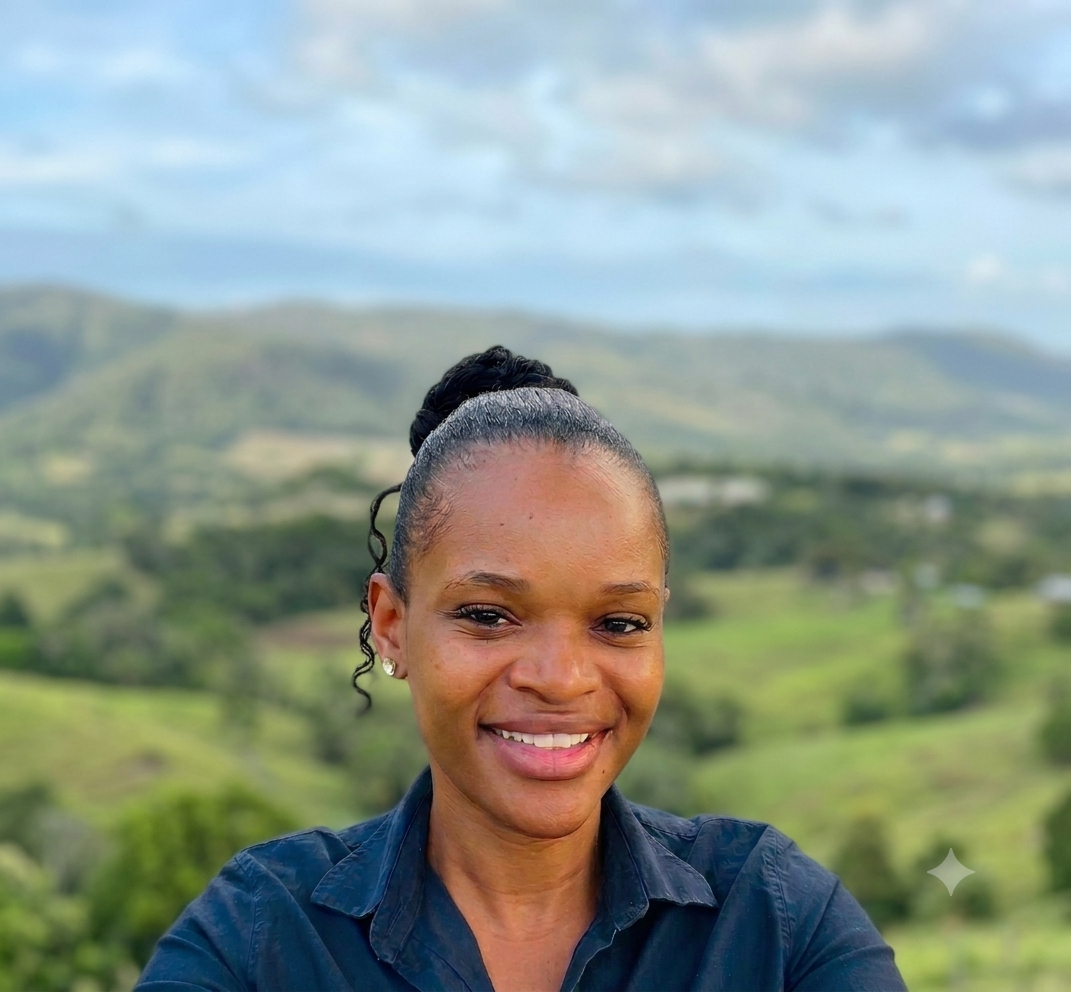 Odwa smiling in a blue shirt with a blurred green mountain landscape behind her