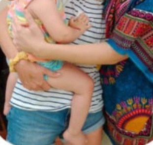 Una mujer carga a un niño pequeño. Ambos visten ropa informal; se ve una camisa con estampado vibrante.