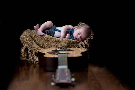 Recién nacido durmiendo sobre una manta dentro de una guitarra, fondo negro, madera marrón.