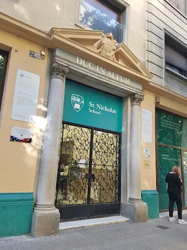 Entrada del Colegio San Nicolás. Puerta verde, columnas blancas, edificio color canela. Una persona de pie a la derecha.