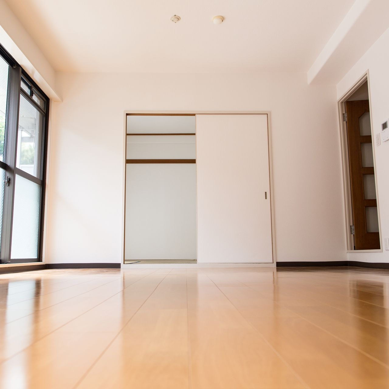 Une pièce vide avec un parquet clair, des murs blancs, un grand placard à porte coulissante et une porte vitrée donnant sur l'extérieur.