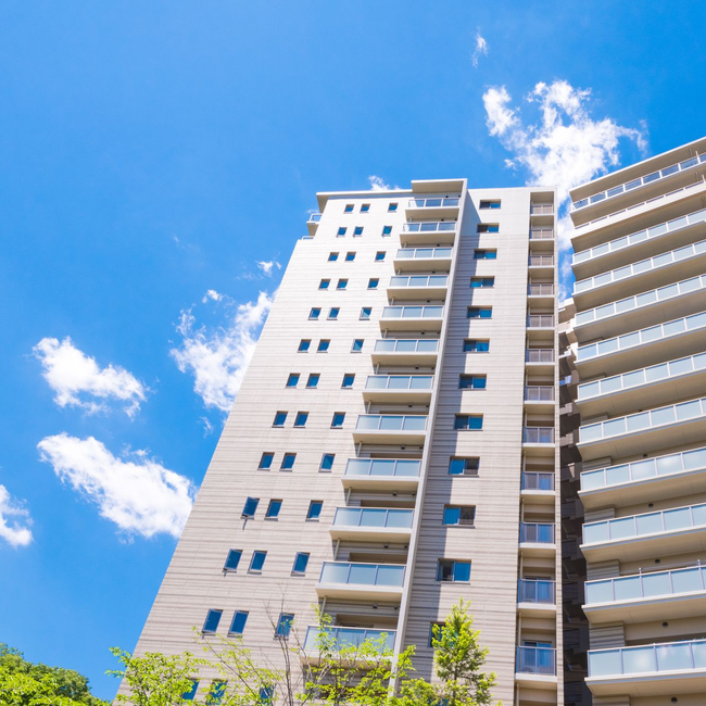 Un immeuble d'appartements moderne à plusieurs étages, avec une façade beige et des balcons, sous un ciel bleu vif parsemé de nuages ​​épars.
