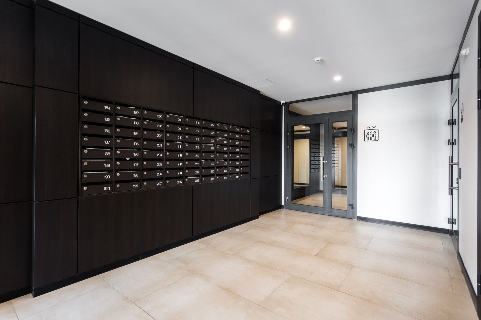 Hall d'entrée moderne d'un immeuble d'appartements avec boîtes aux lettres noires, sol carrelé et portes d'entrée vitrées