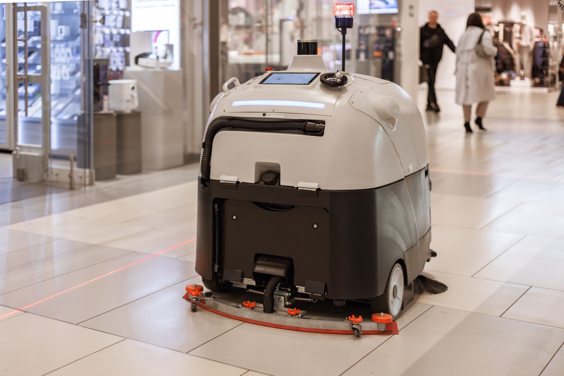 Un robot nettoyeur de sols, blanc et noir, sur le carrelage d'un centre commercial intérieur baigné de lumière.