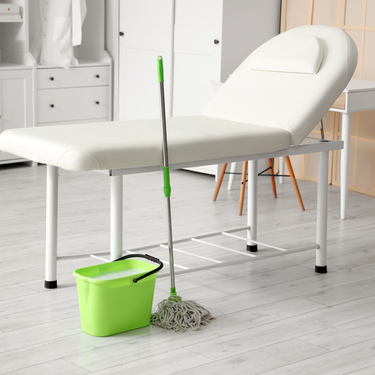 Balai et seau vert à côté d'une table de massage blanche dans une pièce lumineuse.
