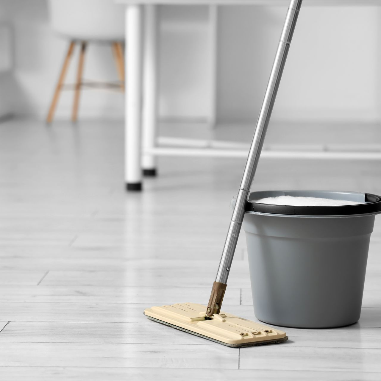 Une serpillière et un seau gris sur un parquet clair dans une pièce lumineuse