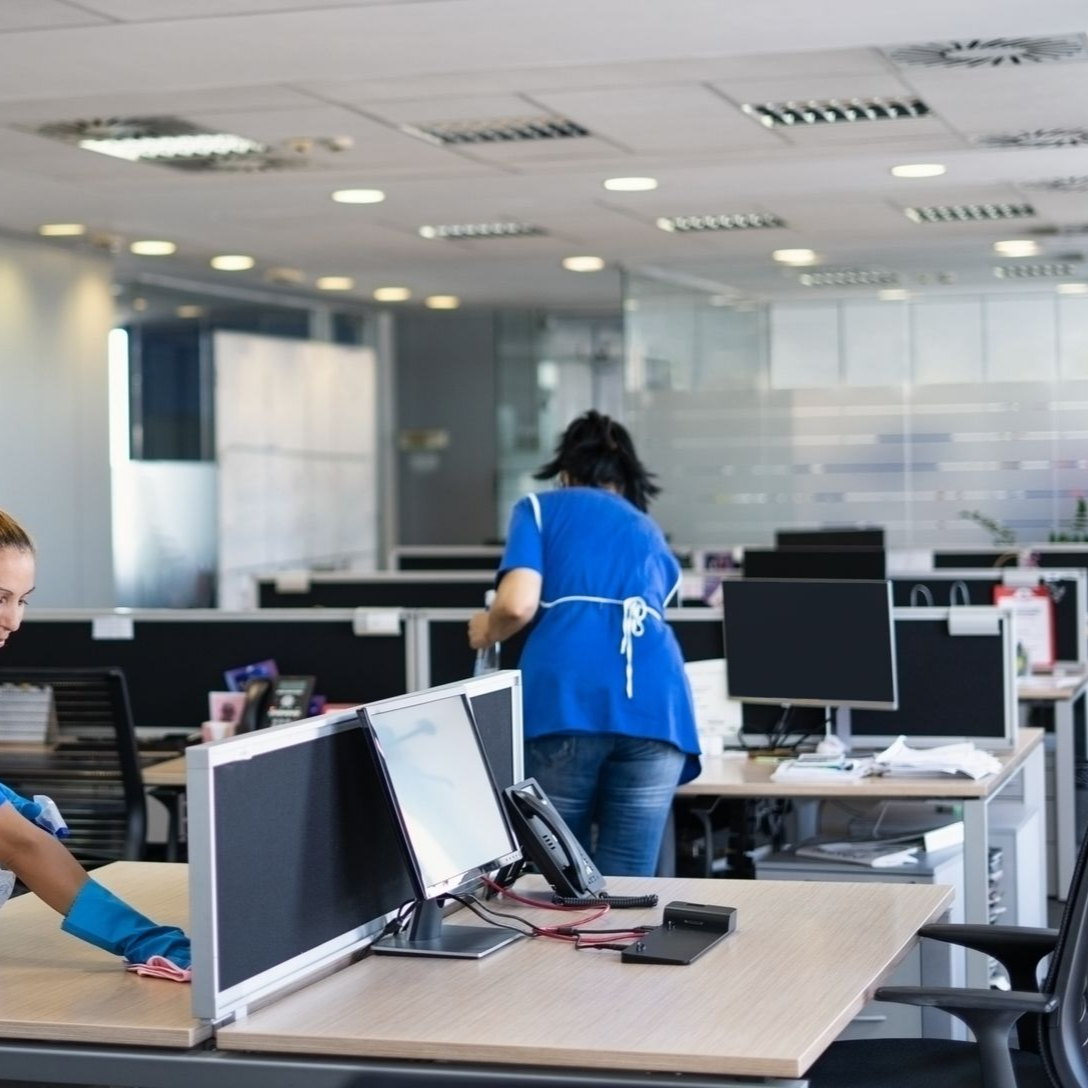 Deux personnes portant des gants de nettoyage bleus nettoient les surfaces des bureaux et les postes de travail.