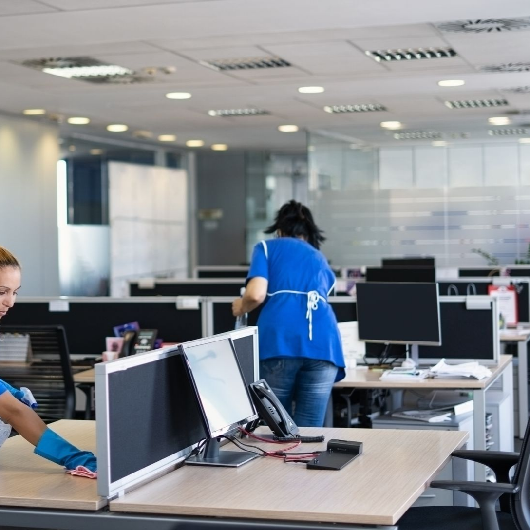 Deux employés nettoient des bureaux dans un bureau équipé de postes de travail et d'un éclairage modernes.
