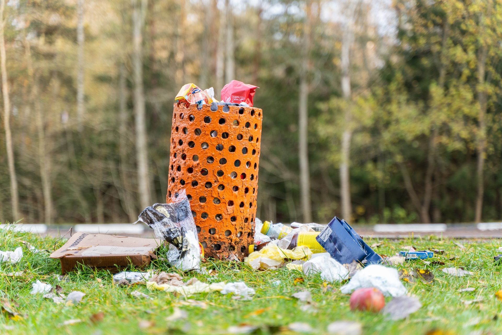 Une poubelle orange débordante sur une pelouse jonchée de détritus.