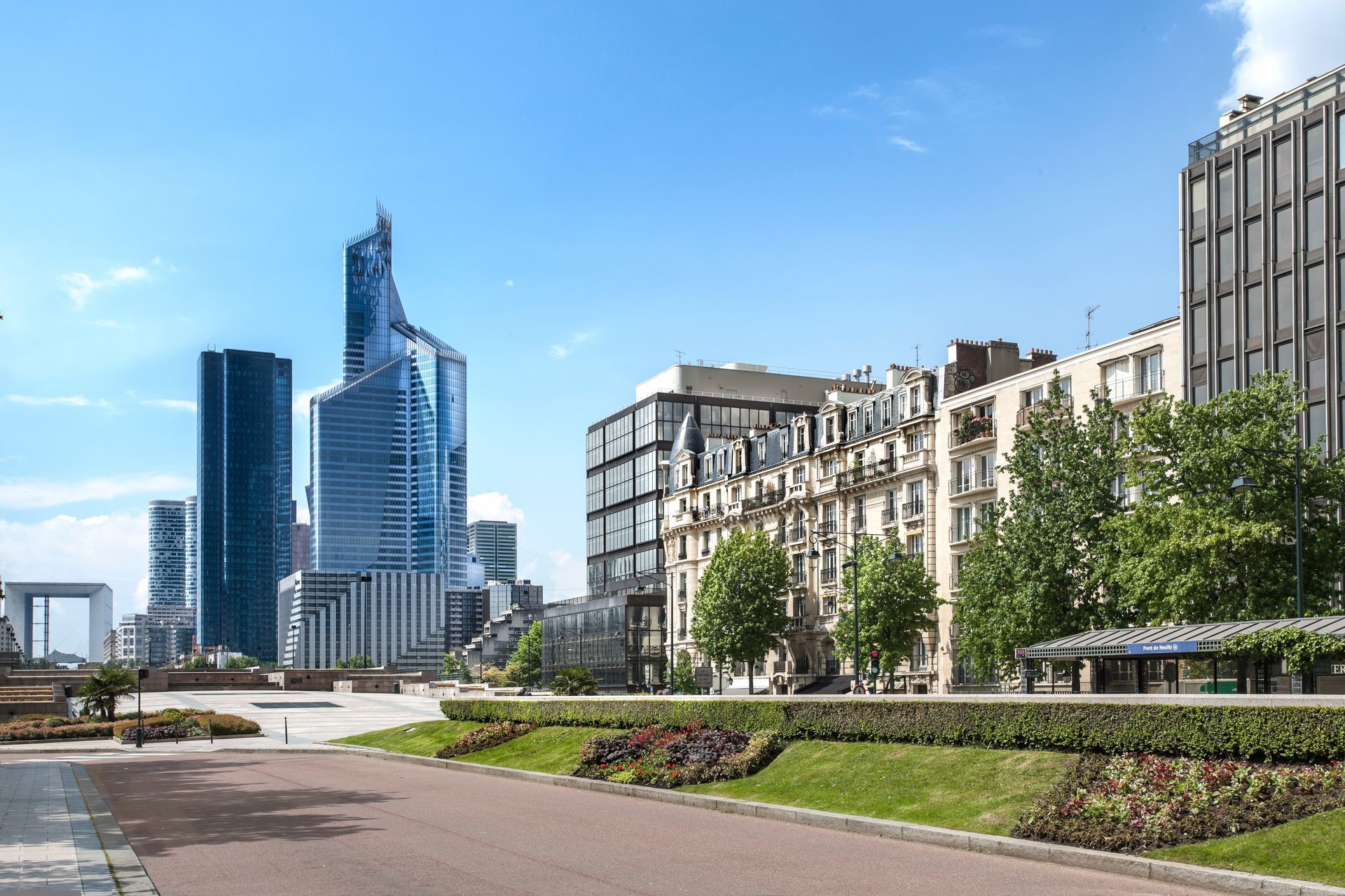 Vue d'une rue de Neuilly-sur-Seine où se côtoient les bâtiments modernes de la Défense aux bâtiments historiques et aux arbres verdoyants d'une allée paysagée.