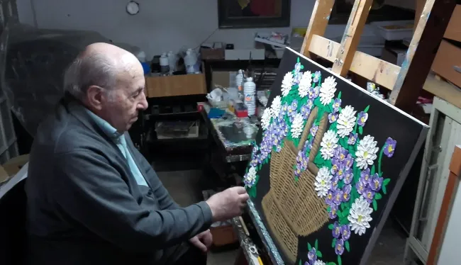 Un hombre está pintando un cuadro de una canasta de flores.