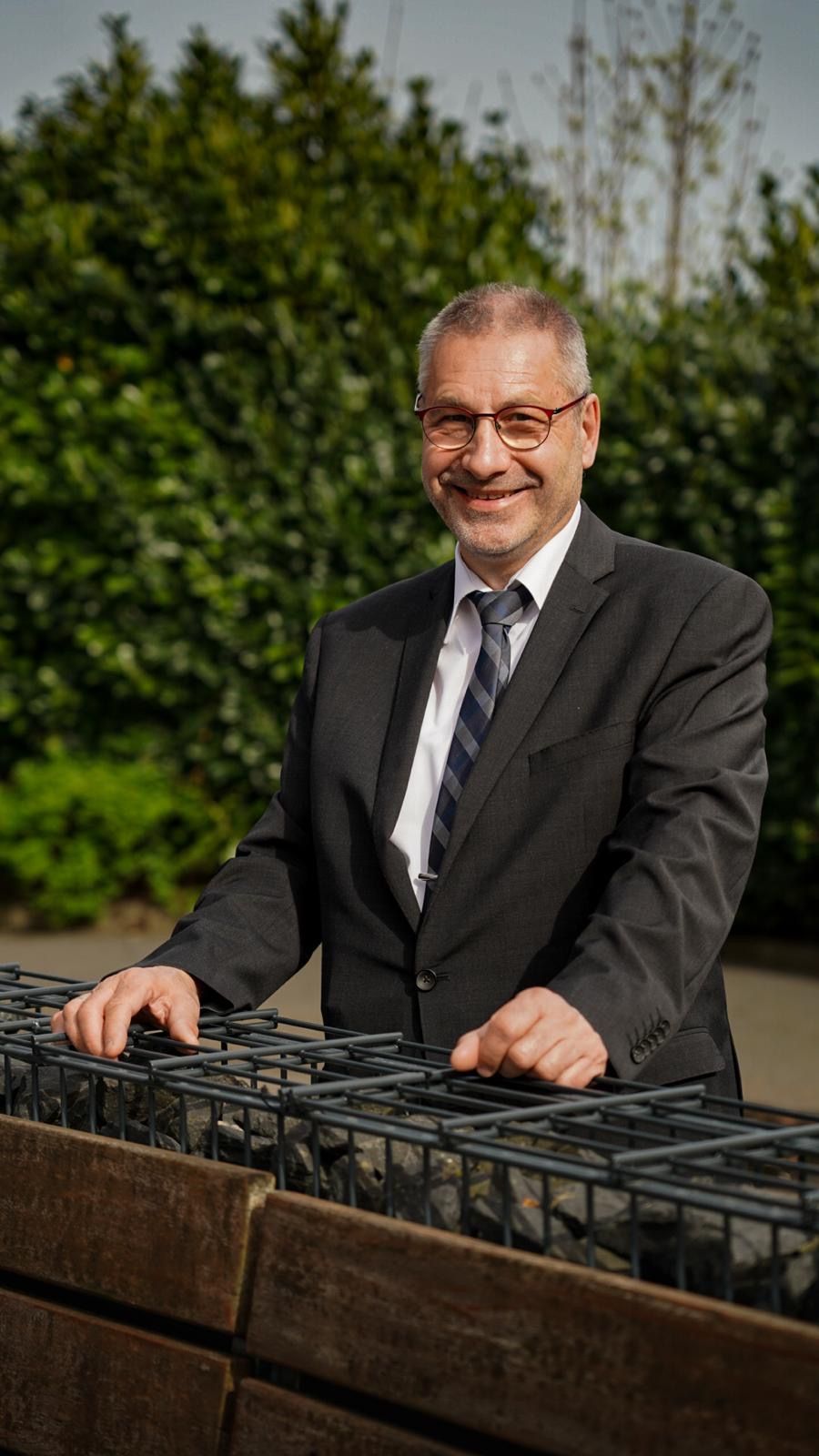 Ein Mann mit Brille und blauem Hemd lächelt und legt die Hand auf sein Kinn.