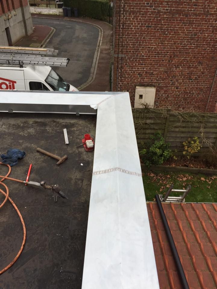 Toit plat avec installation de solins métalliques ; outils et bâtiment en briques visibles.