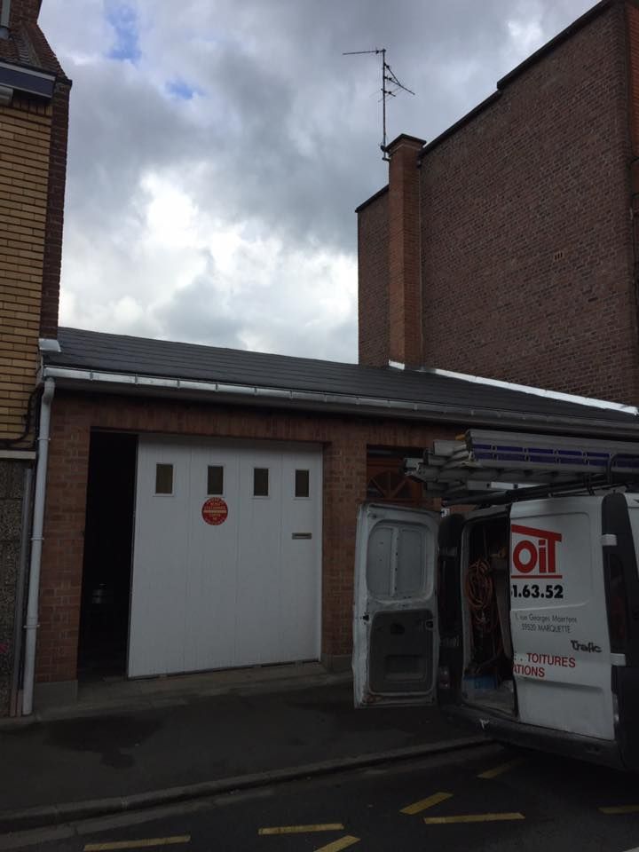 Garage en briques avec porte blanche ; antenne sur la cheminée ; ciel nuageux ; camionnette garée à proximité.