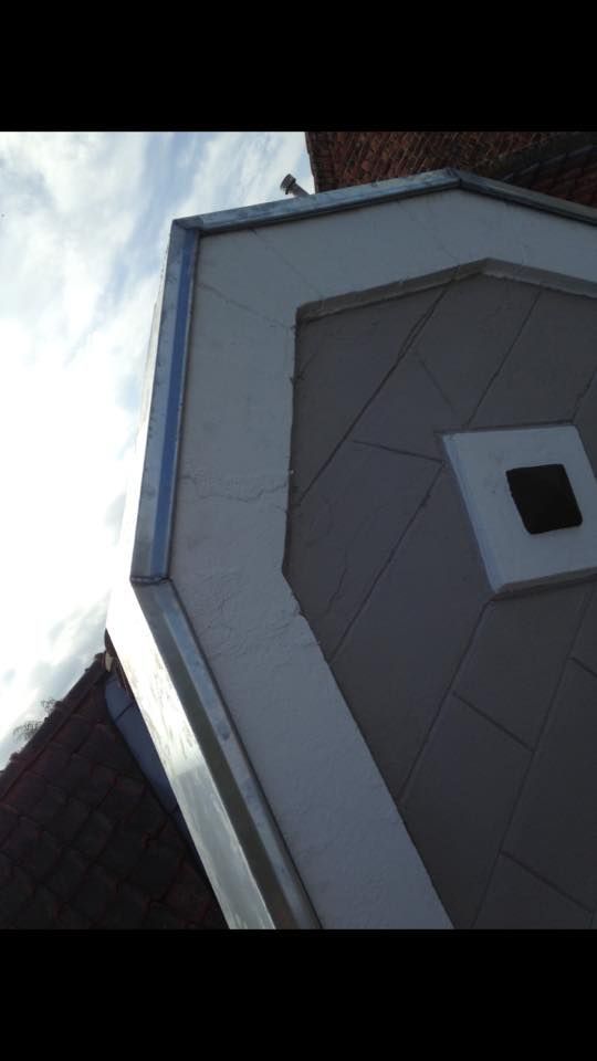 Gros plan sur un coin de toit de maison avec un bardage clair, des bardeaux foncés et un ciel bleu en arrière-plan.