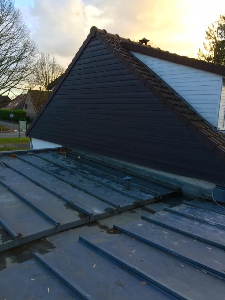 Toit gris foncé avec une façade triangulaire noire. Ciel bleu et arbres en arrière-plan.