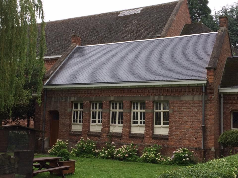 Bâtiment en briques avec de nombreuses fenêtres, un toit en pente et un espace gazonné.