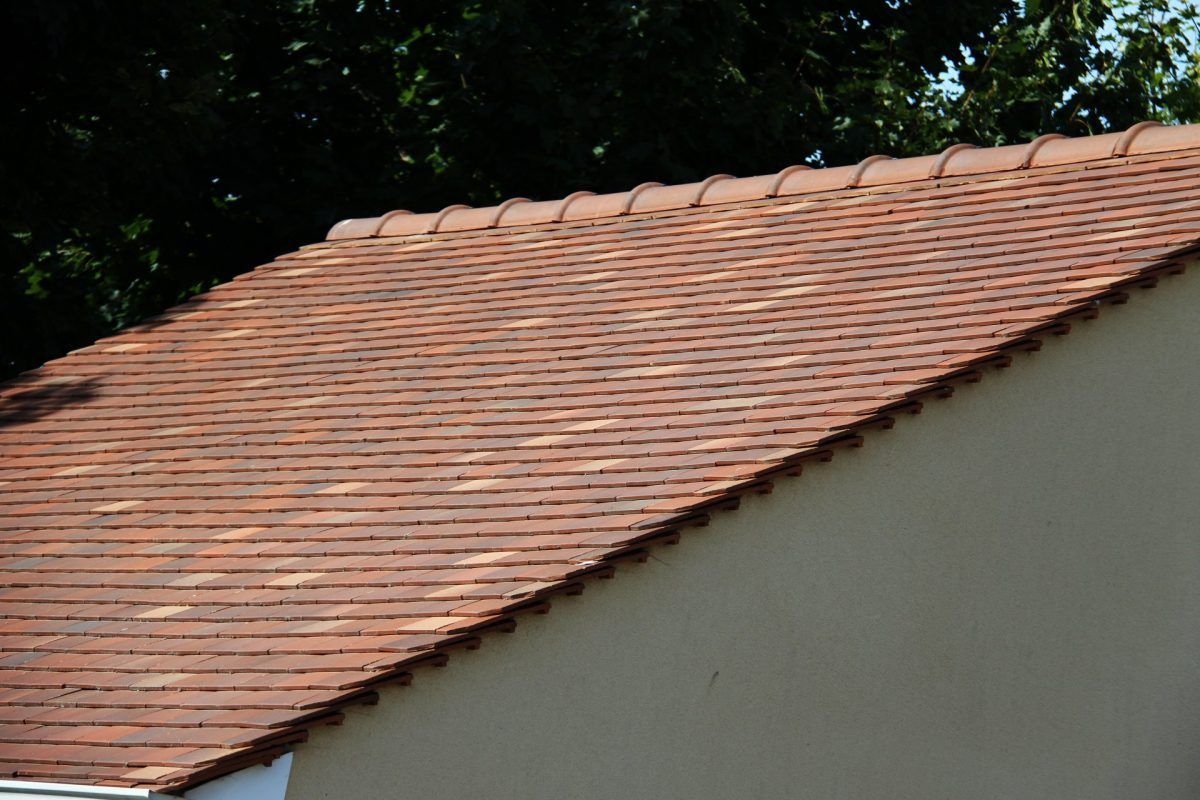 Toit de tuiles rouges sur un bâtiment couleur crème, avec du feuillage vert en arrière-plan.