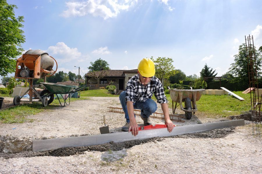 Ouvrier du bâtiment portant un casque jaune utilise un niveau pour vérifier une fondation en béton.
