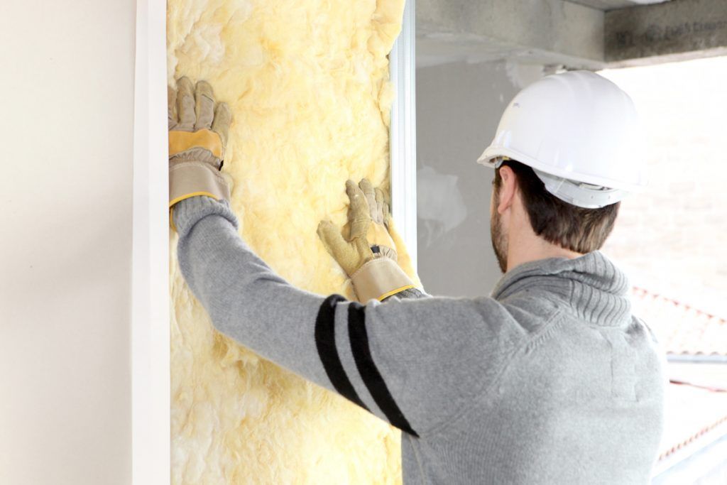 Ouvrier du bâtiment installant de l'isolant dans un mur, portant des gants et un casque de chantier.