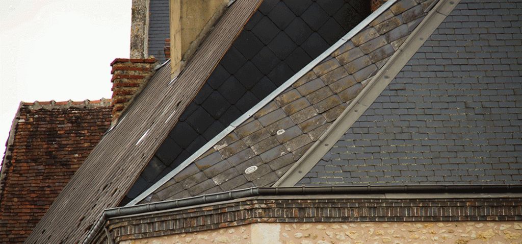 Un bâtiment au toit de tuiles gris foncé. Une cheminée en briques est visible dans un coin.