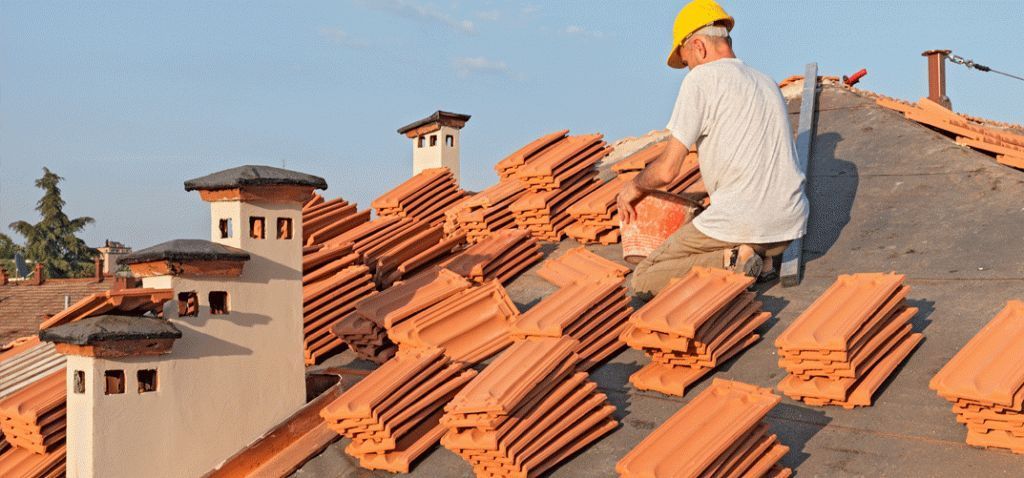 Un ouvrier portant un casque de chantier jaune pose des tuiles en terre cuite sur un toit.
