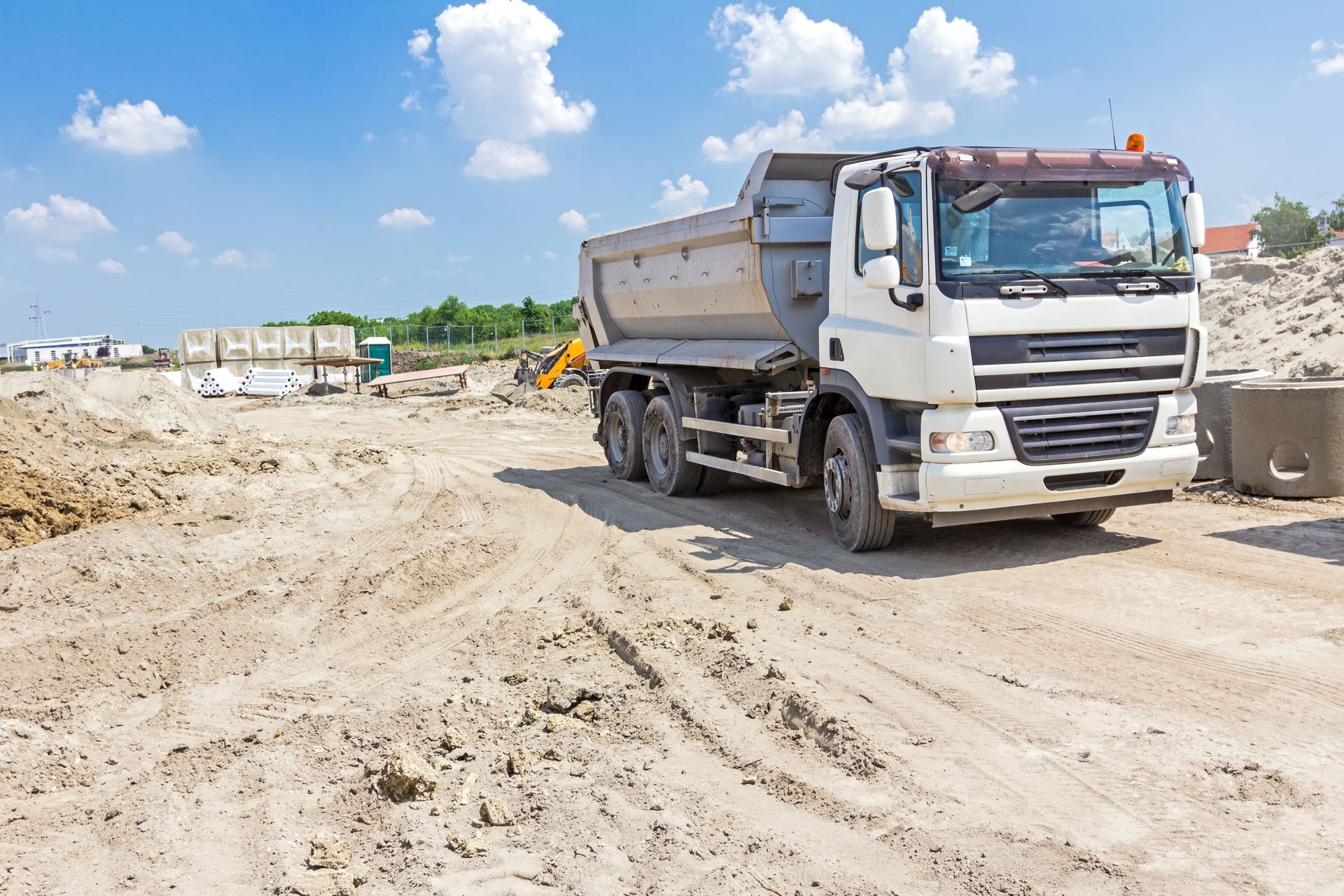 Un camion-benne blanc garé sur un chantier poussiéreux sous un ciel d'un bleu éclatant.