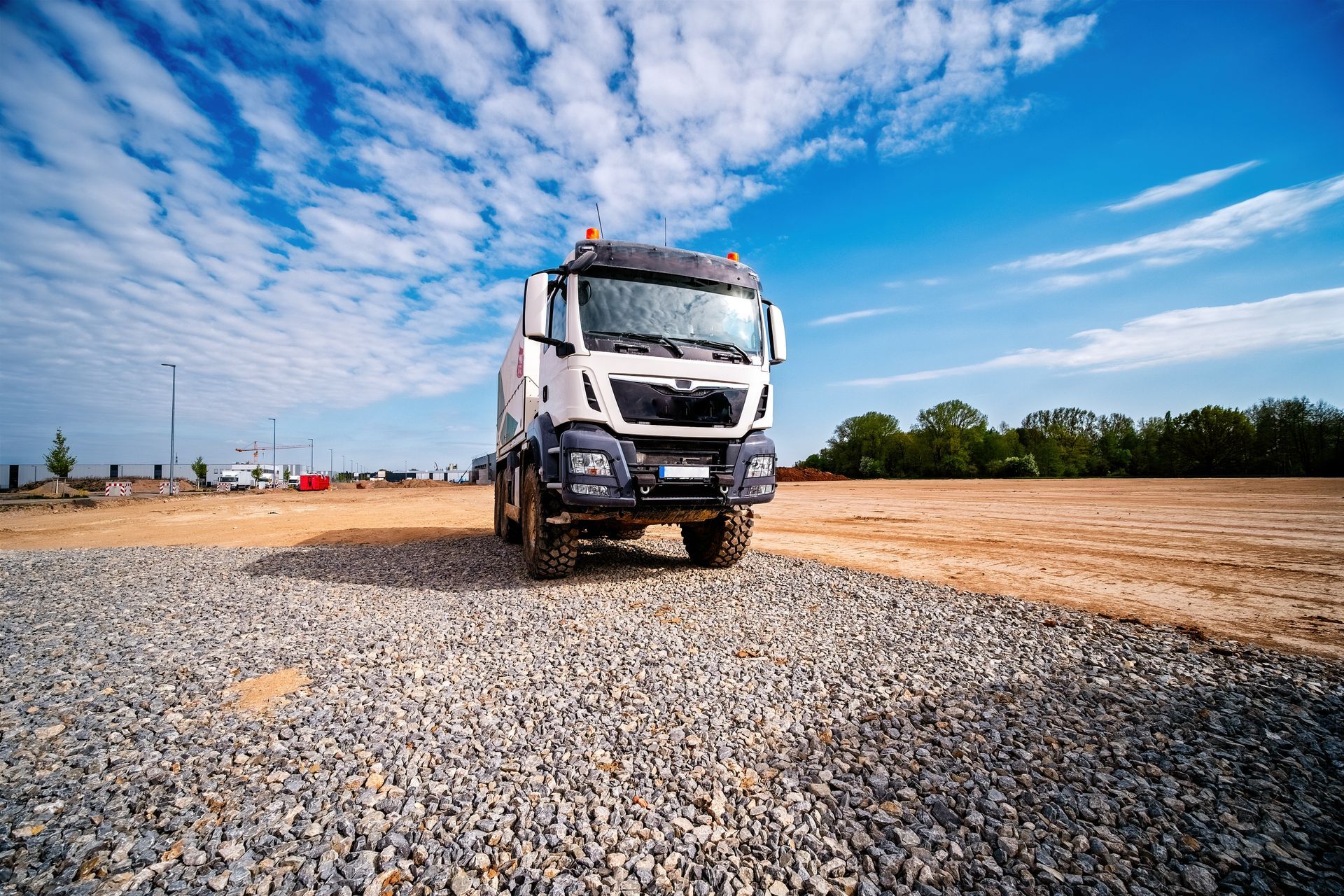 Un camion-benne blanc stationné sur une surface de gravier sous un ciel bleu éclatant parsemé de nuages ​​épars.