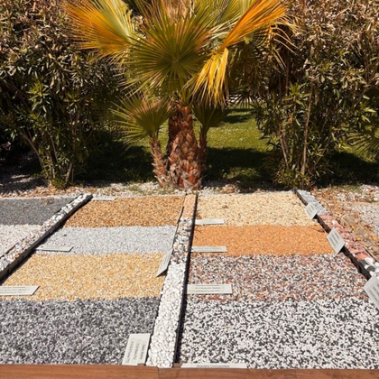 Une présentation d'échantillons de gravier et de pierres de différentes couleurs, disposés en grille au sol.